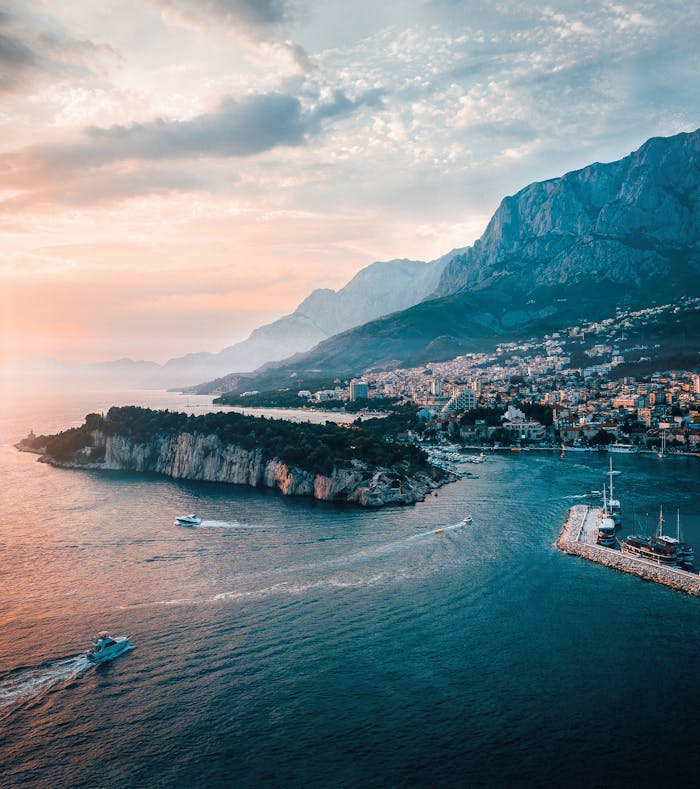 Scenic aerial shot of Makarska, Croatia capturing the coastline, island, and majestic mountains at sunset.